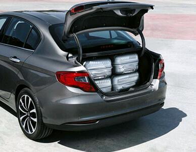 Szary sedan z otwartym bagażnikiem wypełnionym czterema srebrnymi walizkami na kółkach.