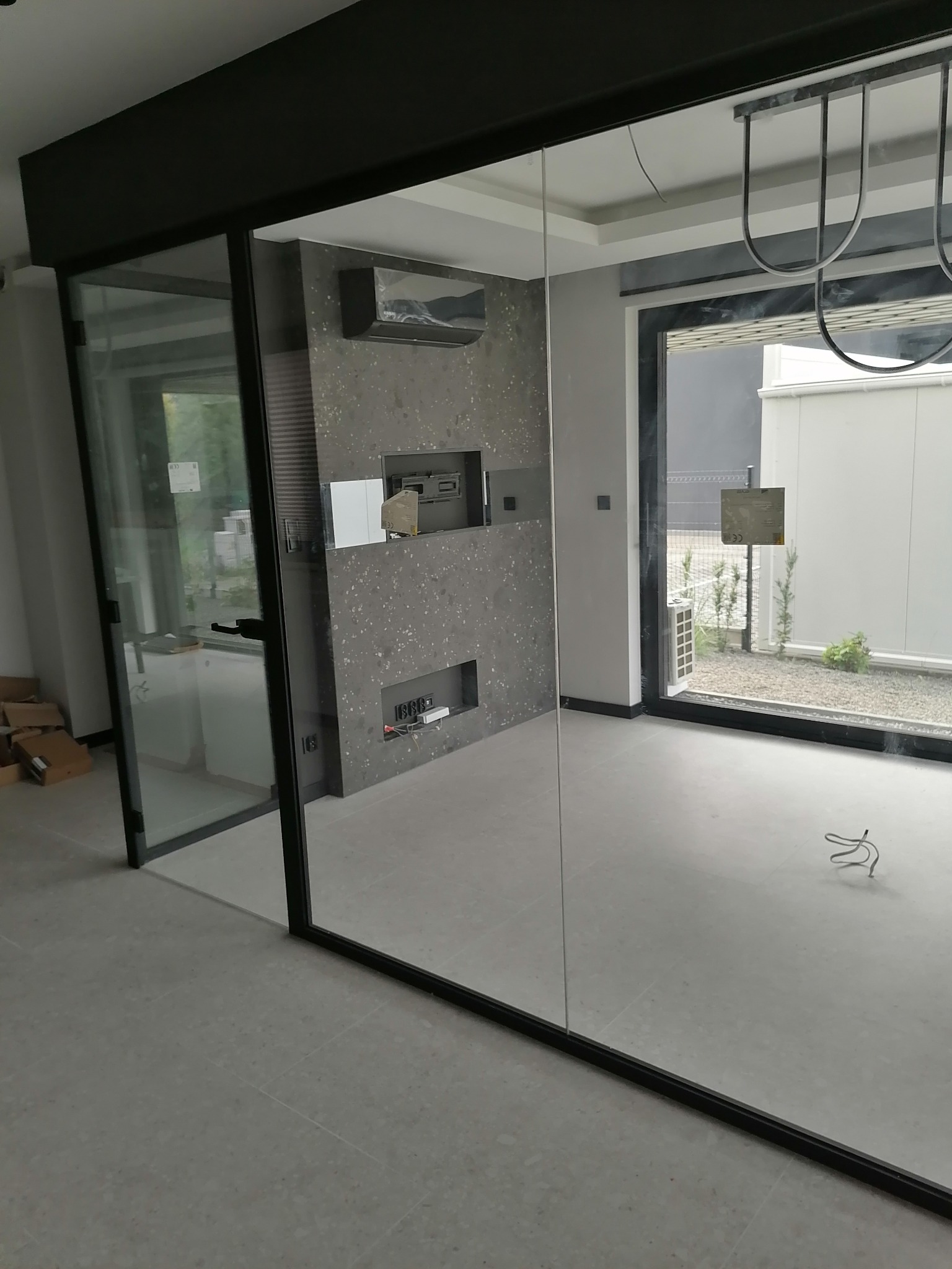 Nowoczesne wnętrze z szarą ścianą dekoracyjną, czarnymi ramami okien i szklanymi drzwiami przesuwnymi. Minimalistyczny design w jasnej przestrzeni.