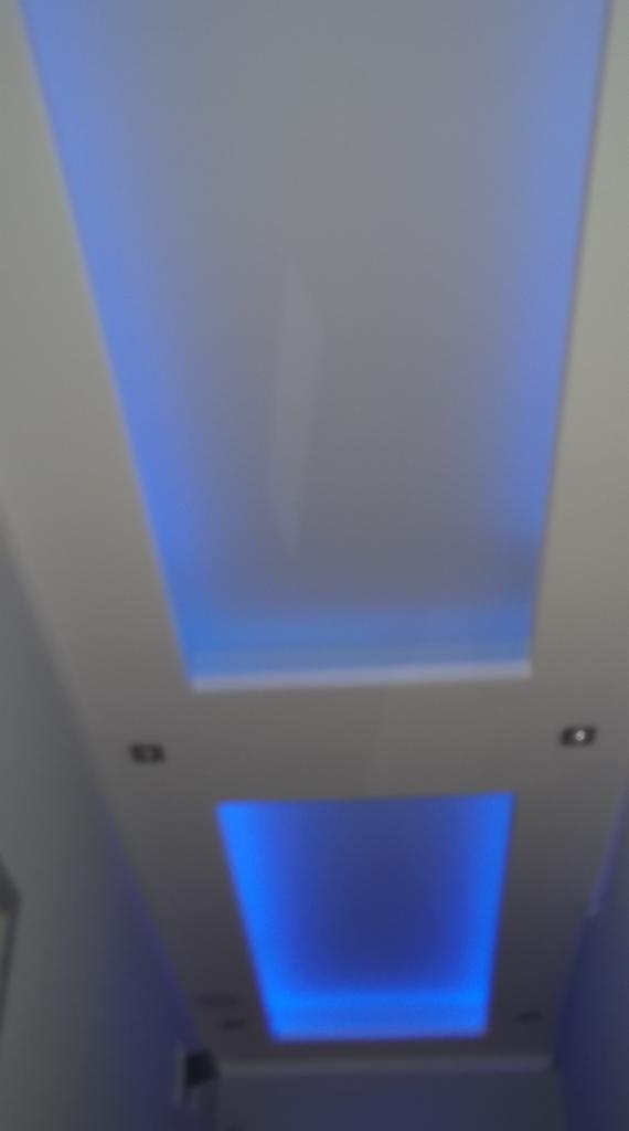 Podwieszany sufit z dwoma prostokątnymi wnękami oświetlonymi niebieskim światłem LED, widok z dołu pod kątem.