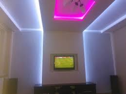 Salon z podświetlanym sufitem w kolorze różowym i białym, telewizor w ramie, nowoczesne oświetlenie LED wzdłuż ścian.