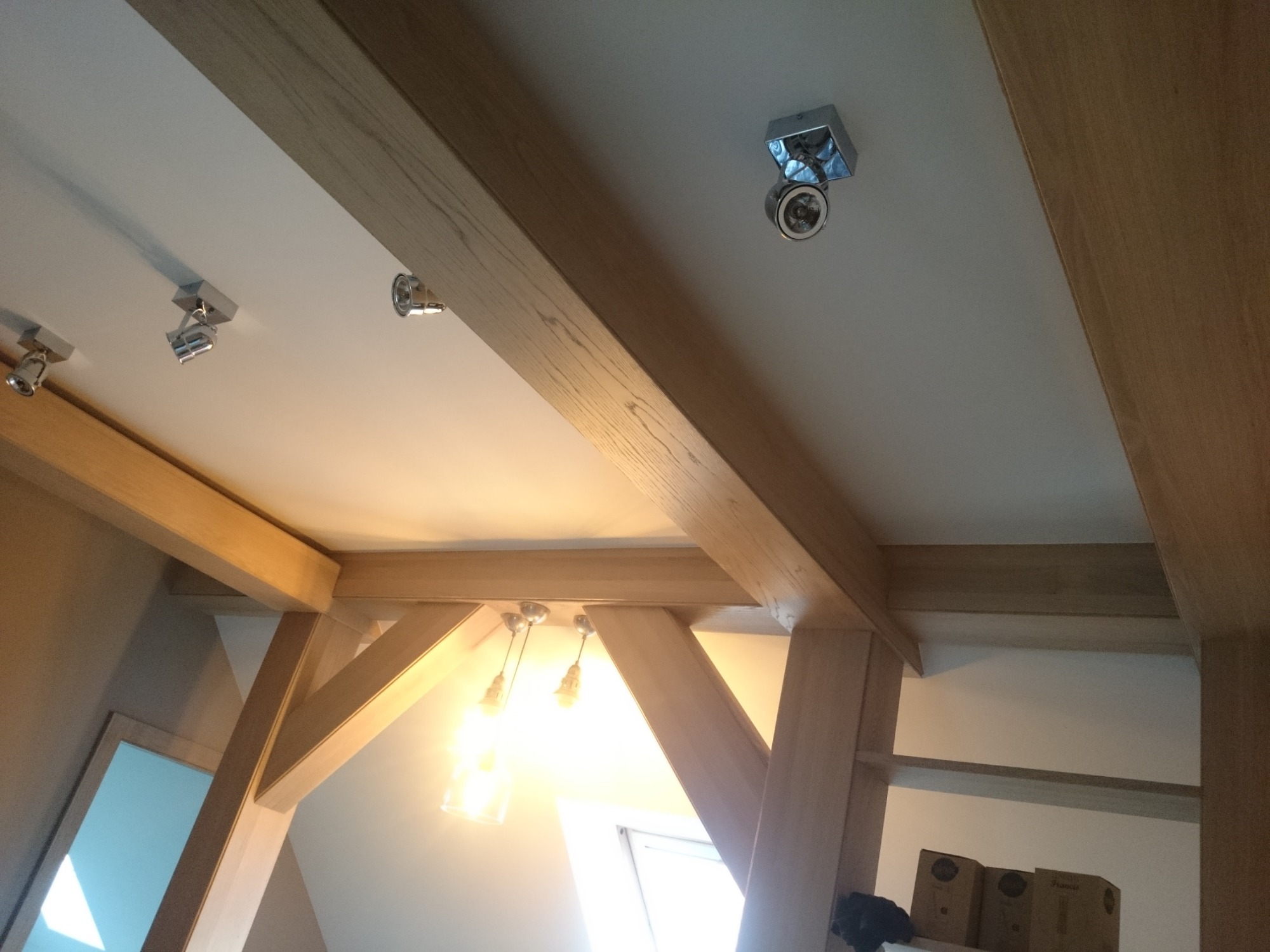 Drewniane belki stropowe w jasnym wnętrzu w Gdyni, z widocznymi punktowymi lampami sufitowymi i oknem w tle.