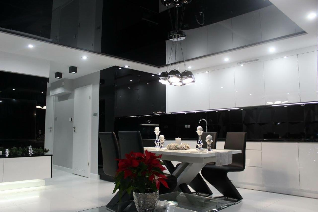 Nowoczesna kuchnia w czerni i bieli z błyszczącym sufitem, oświetleniem punktowym i wiszącą lampą nad stołem jadalnym, uzupełniona dekoracjami świątecznymi.