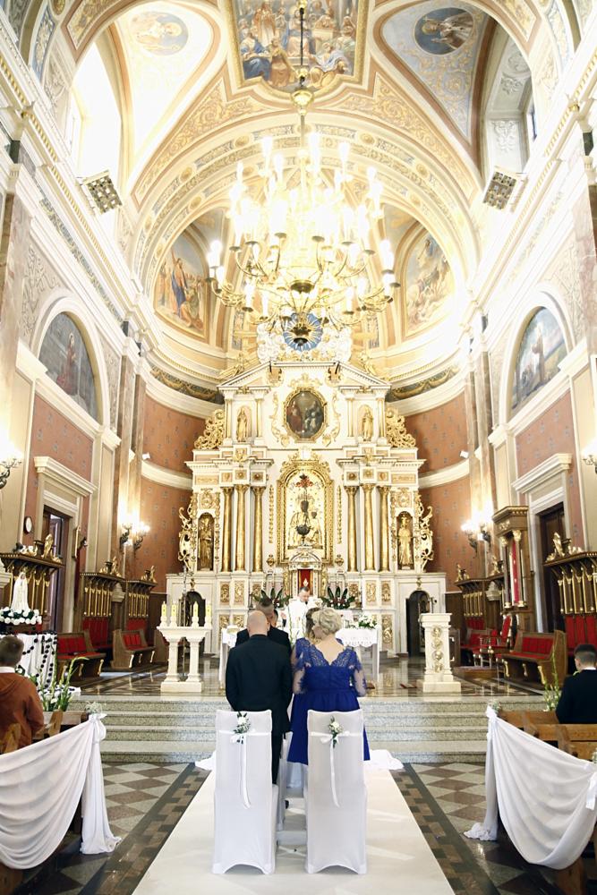 Wnętrze kościoła z parą młodą podczas ceremonii ślubnej, widok na ołtarz i zdobione sklepienie.