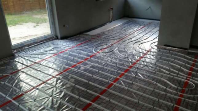 Rozłożona instalacja ogrzewania podłogowego na folii izolacyjnej z czerwonymi liniami pomocniczymi w surowym stanie, przed wylewką.