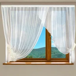 Delikatna, biała, zwiewna zasłona woalowa zawiązana na kokardę, z dekoracyjnym marszczeniem z boku okna z widokiem na zalesione wzgórza i błękitne niebo.