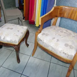 Odnowione krzesło i podnóżek z drewnianą ramą, obite jasną tkaniną w kwiatowy wzór, wykończone złotą lamówką. Widoczne detale rzeźbione w drewnie.