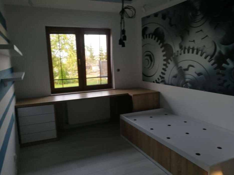 Pokój młodzieżowy z biurkiem narożnym zintegrowanym z parapetem, szafką i łóżkiem, na ścianie fototapeta z motywem zębatek.