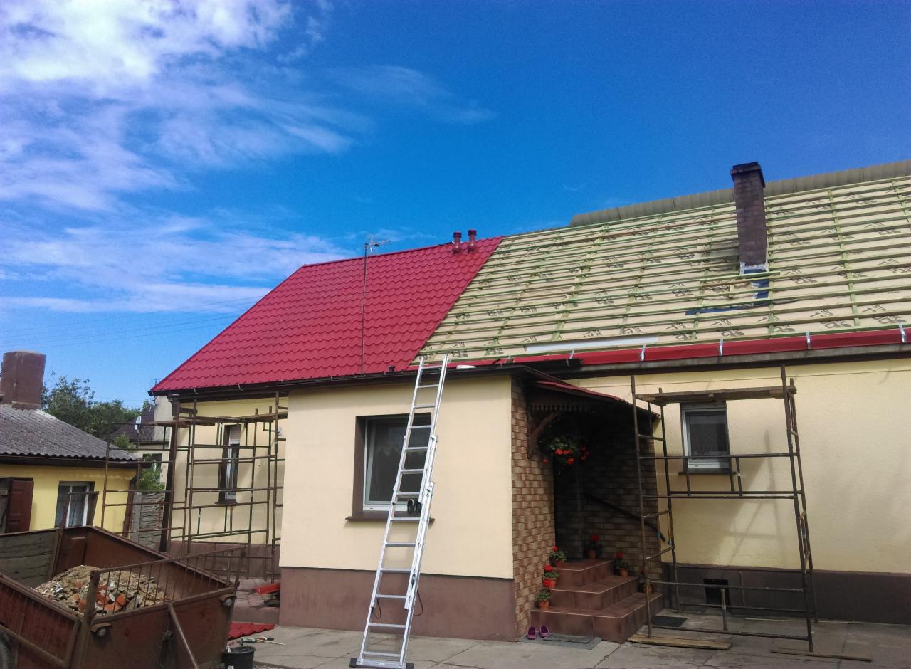 Dom z częściowo wymienionym, czerwonym dachem z blachy trapezowej, widoczne rusztowania i drabina oparta o ścianę, przygotowane łatowanie pod resztę pokrycia.