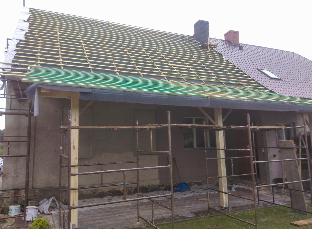 Etap wymiany dachu z widoczną konstrukcją drewnianą, membraną dachową i częściowo ułożoną blachodachówką, rusztowania wokół budynku.