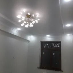 Jasne wnętrze pokoju po remoncie z nowoczesnym oświetleniem sufitowym, białymi ścianami, oknem z brązową ramą i grzejnikiem.