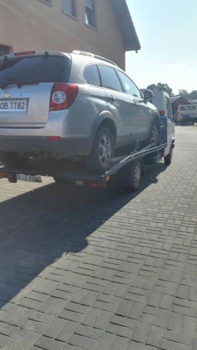 Srebrny SUV Chevrolet Captiva z polską tablicą rejestracyjną na platformie lawety, widok z tyłu, ceglana kostka brukowa na pierwszym planie.