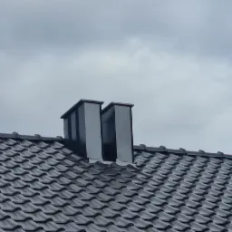 Grafitowy dach z dachówki ceramicznej z dwoma kominami wentylacyjnymi na tle pochmurnego nieba z prześwitami błękitu.