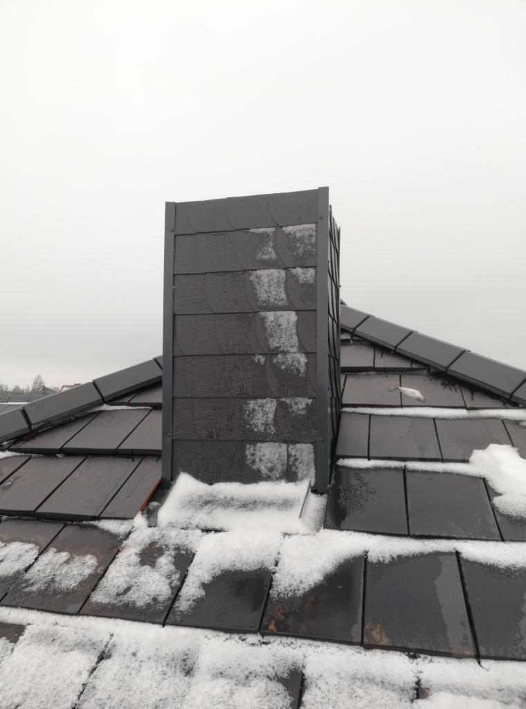 Grafitowy dach pokryty łupkiem z widocznym kominem w obudowie, lekko ośnieżony, pochmurne niebo w tle.