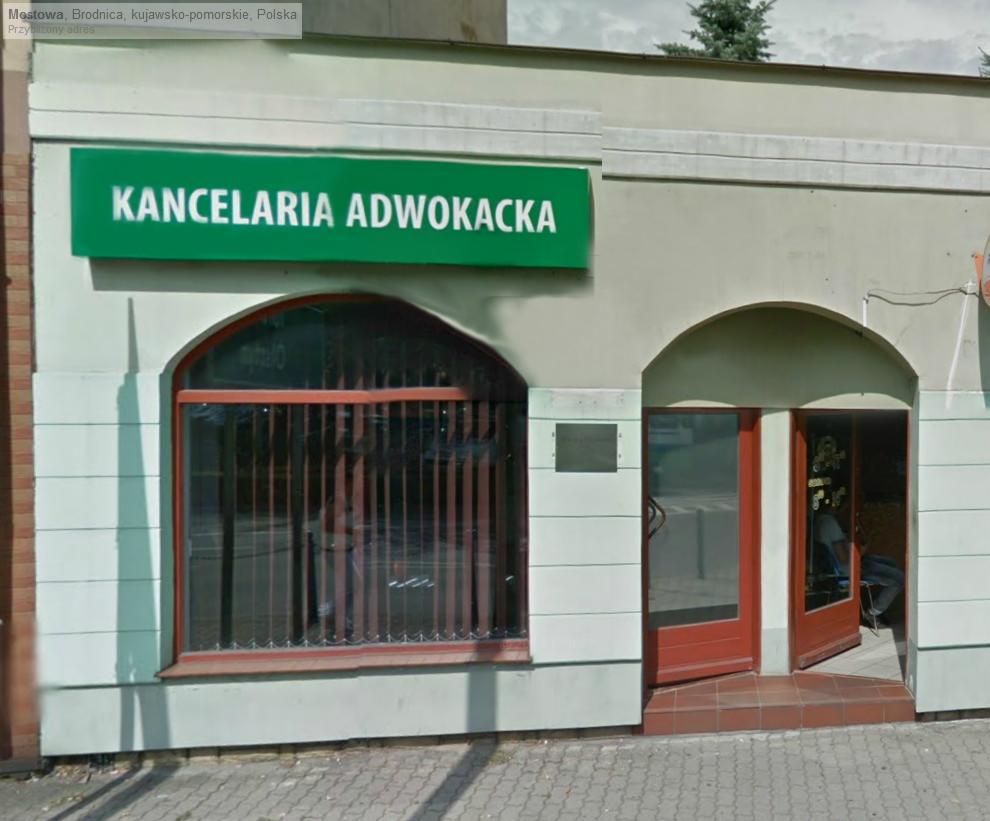 Fasada budynku z zielonym szyldem 'Kancelaria Adwokacka' nad oknem z kratami i otwartymi drzwiami wejściowymi.