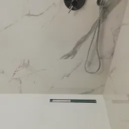 Nowoczesna kabina prysznicowa z odpływem liniowym i marmurowymi płytkami, widok z góry na chromowaną baterię i słuchawkę prysznicową.