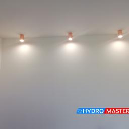 HYDROMASTERS - Trzy punktowe lampy sufitowe z brązowymi obudowami, oświetlające białe ściany w pomieszczeniu; widoczne logo firmy Hydro Masters w dolnej części kadru.