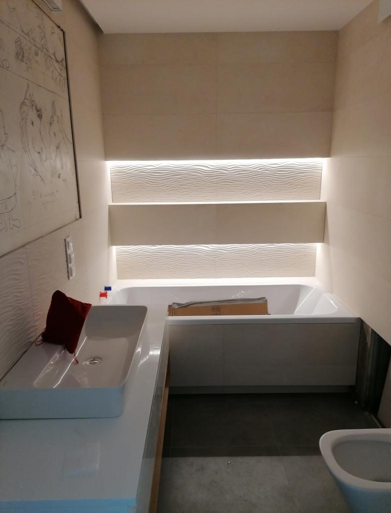 Nowoczesna łazienka z podświetlanymi półkami nad wanną, umywalką nablatową i dekoracyjną grafiką na ścianie.