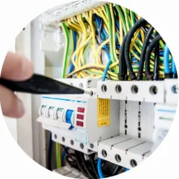 Instalator dokręca śrubę w rozdzielnicy elektrycznej marki Hager, widoczne kolorowe przewody i zabezpieczenia