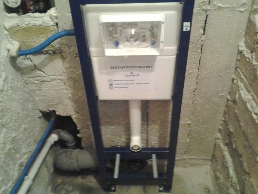 Stelaż podtynkowy Cersanit zamontowany w surowym stanie łazienki, widoczne nieotynkowane ściany i instalacje wodne przed zabudową.