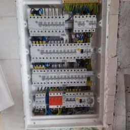 Rozdzielnica elektryczna z zainstalowanymi bezpiecznikami i przewodami, zamontowana w surowej ścianie z betonu komórkowego, widoczne elementy instalacji odgromowej.