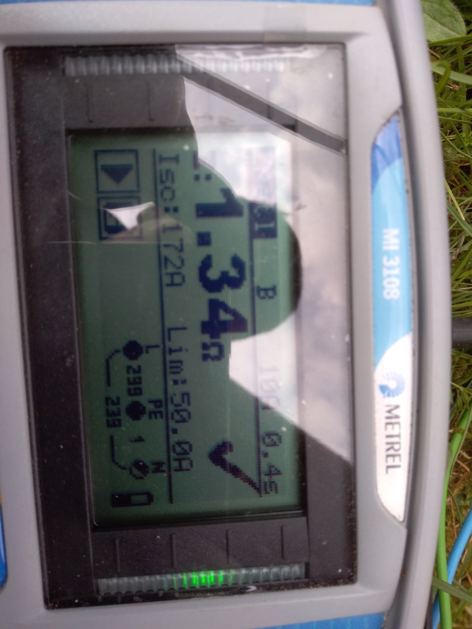 Wyświetlacz miernika elektrycznego Metrel MI 3108 z widocznymi wynikami pomiarów prądu zwarciowego (Isc: 1.72A) i impedancji pętli zwarcia (Lim: 50.0A) na tle trawy.