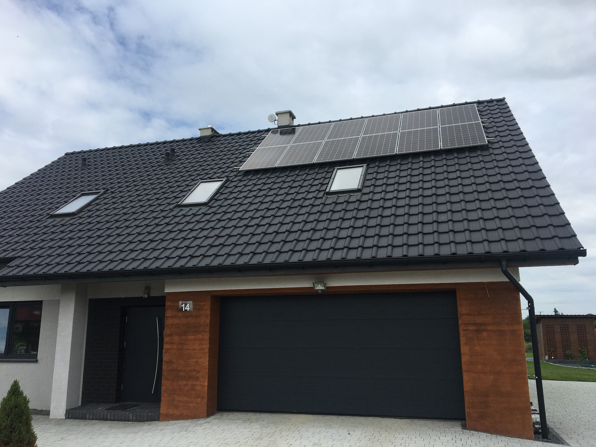Panele fotowoltaiczne zamontowane na dachu nowoczesnego domu jednorodzinnego w Ziębicach, widoczne okna dachowe i ciemna dachówka.