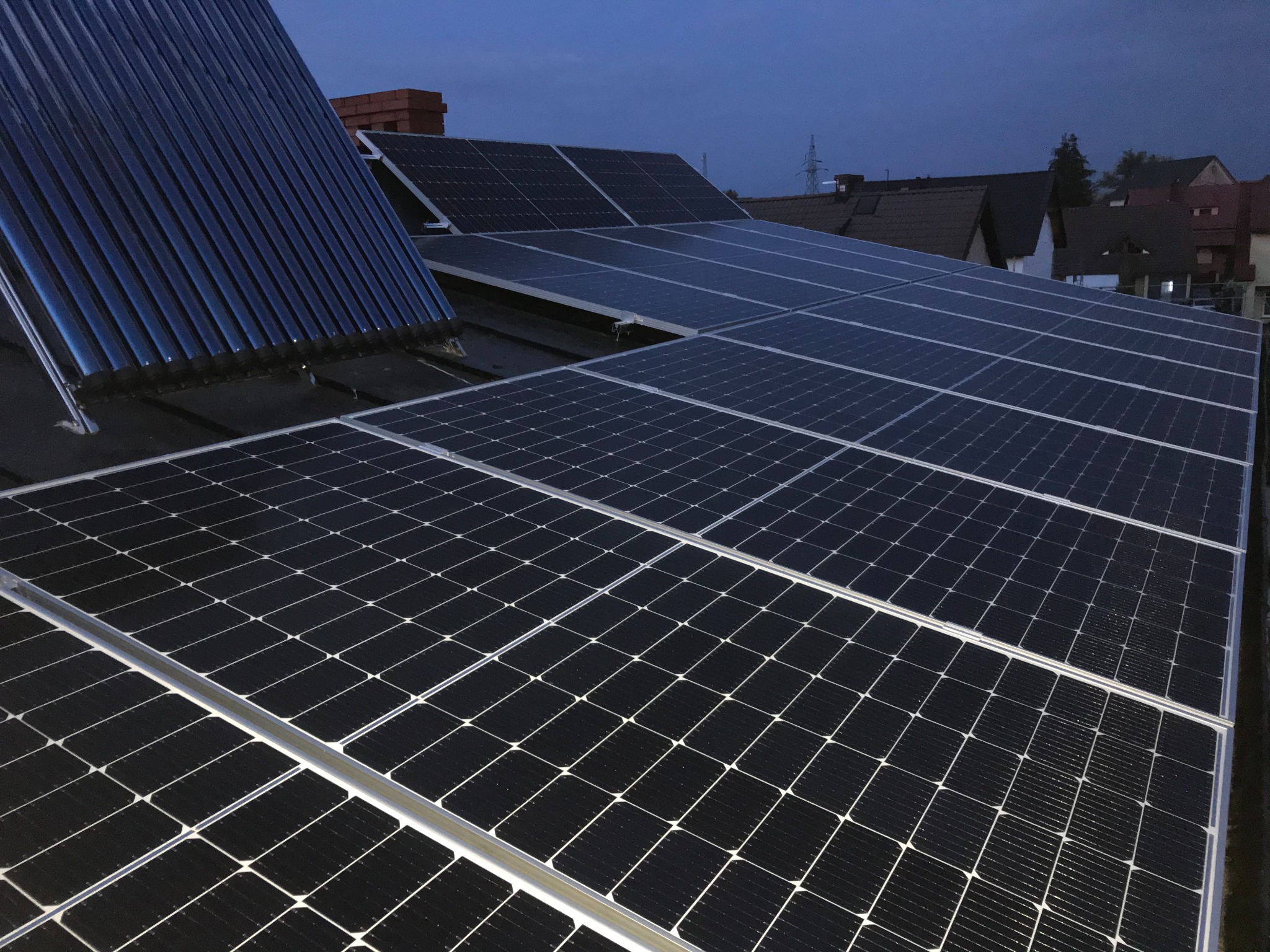 Panele fotowoltaiczne i kolektory słoneczne zamontowane na dachu domu jednorodzinnego, widoczne w wieczornym świetle.