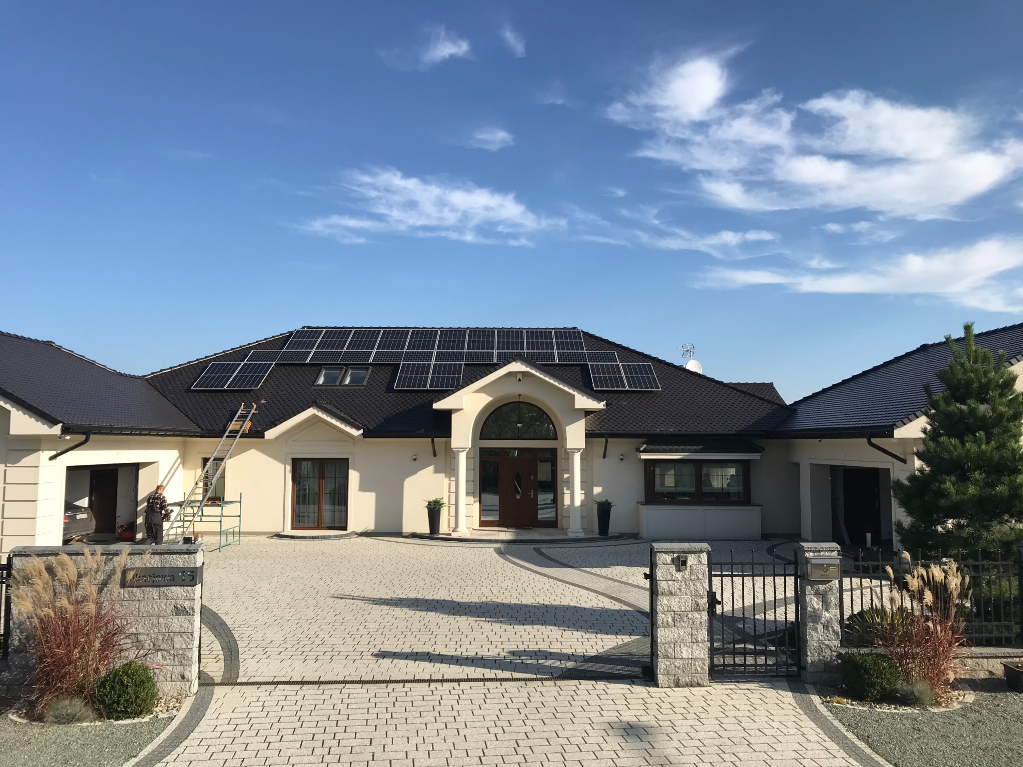 Duży, nowoczesny dom jednorodzinny z panelami słonecznymi na dachu i drabina oparta o ścianę przy garażu.