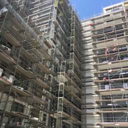 Macrotech Sp z o.o. Sp. Komandytowa - Wielopiętrowy budynek w trakcie prac elewacyjnych, otoczony rusztowaniami, z pracownikami w strojach roboczych na różnych poziomach.