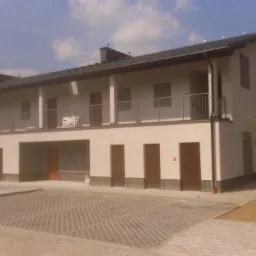 Nowo wybudowany, dwukondygnacyjny budynek mieszkalny wielorodzinny z balkonami, świeżo po zakończeniu prac, z ułożoną kostką brukową na parkingu przed budynkiem i przygotowanym terenem pod trawnik.