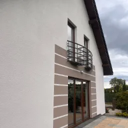 Wykończona elewacja domu jednorodzinnego z balkonem, z dekoracyjnymi pasami w odcieniach brązu, widok z boku, z kostką brukową na pierwszym planie.