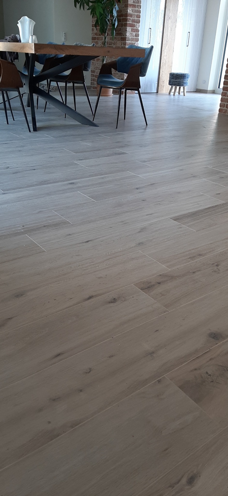 Ułożona podłoga z płytek imitujących drewno w jadalni z nowoczesnym stołem i krzesłami w tle.