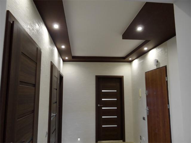 Korytarz z trzema parami drzwi w odcieniach brązu, oświetlenie punktowe w podwieszanym suficie z ciemnego drewna, ściany pokryte dekoracyjnym tynkiem.