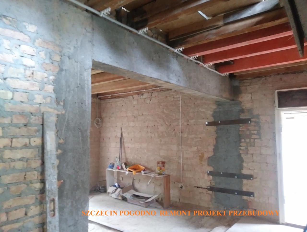 Wnętrze w trakcie remontu z widoczną stalową belką nośną i wzmocnieniami ściany z cegły, częściowo otynkowanej, z widocznymi elementami instalacji elektrycznej.