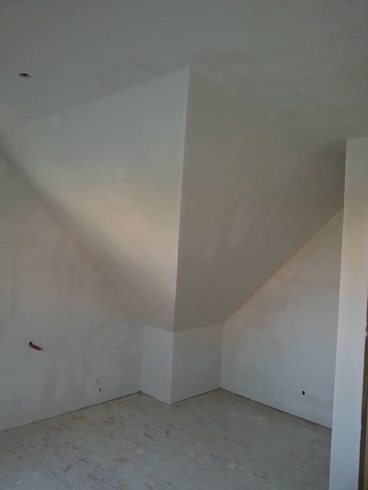 Poddasze po nałożeniu gładzi gipsowej, widoczne nierówności i przygotowanie do dalszych prac wykończeniowych, surowe wnętrze z widocznym punktem świetlnym na suficie.