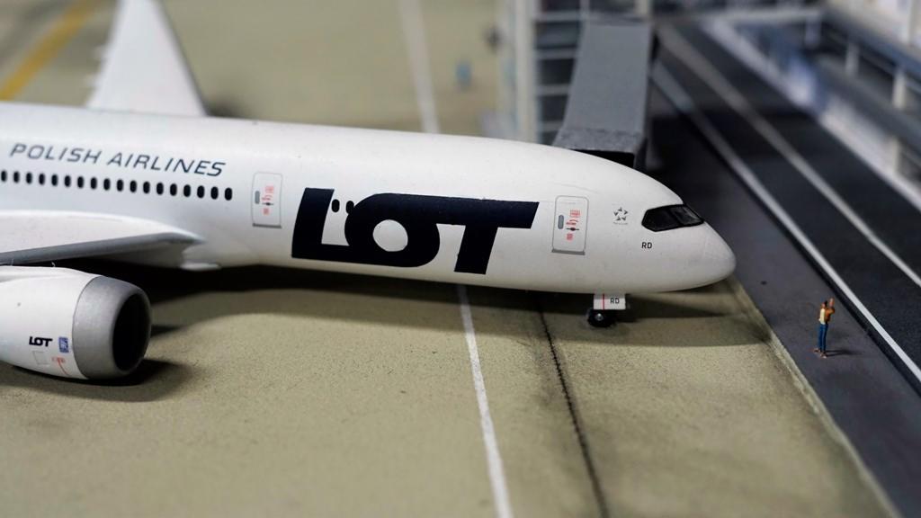 Makieta samolotu LOT Polish Airlines na lotnisku, z miniaturową figurką osoby stojącej obok.