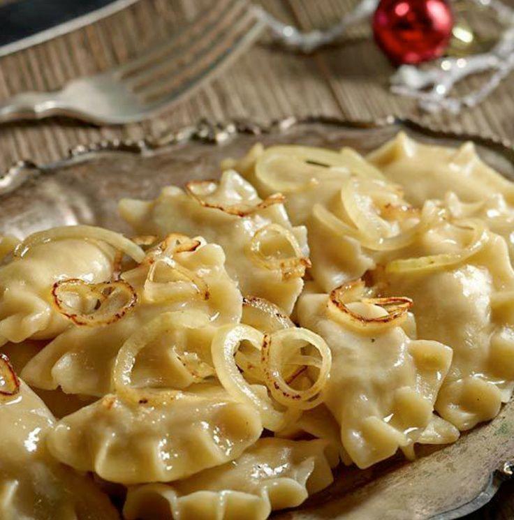 Domowe pierogi okraszone podsmażaną cebulką, ułożone na srebrnej paterze, w tle widoczny widelec i świąteczna bombka.