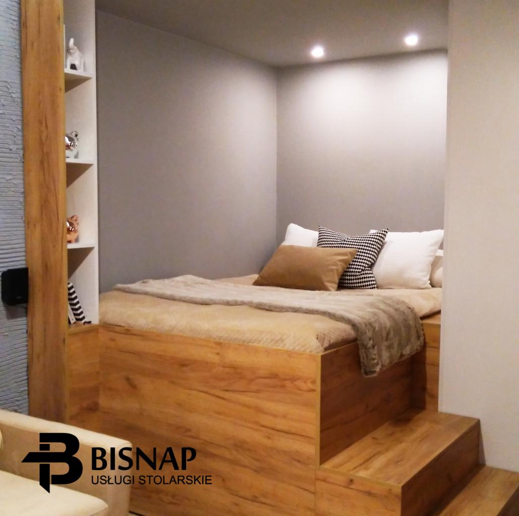 Drewniana antresola sypialna z wbudowanymi schodkami i półkami, oświetlona punktowo, z widocznym logo firmy stolarskiej Bisnap.