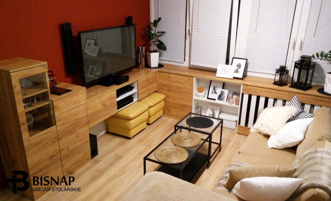 Nowoczesny salon z zabudową meblową z drewna w ciepłym odcieniu, obejmującą szafkę RTV, regał i szafę witrynową; żółte pufy dodają akcentu kolorystycznego.