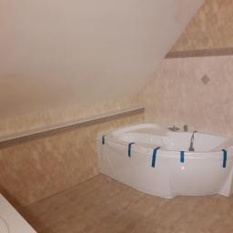 BK Wilbud Sp. z o.o. - Narożna wanna akrylowa zabezpieczona folią malarską w łazience na poddaszu z beżowymi płytkami ściennymi i podłogowymi.