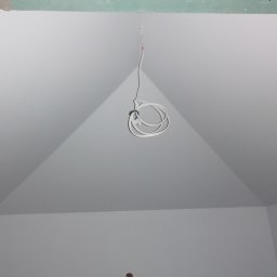 Usługi Ogólnobudowlane Dawid Niełacny - Wnętrze pokoju z pomalowanymi na biało ścianami i skośnym sufitem, widoczne wystające przewody elektryczne.