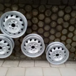 Cztery stalowe felgi samochodowe po obróbce, prawdopodobnie malowane proszkowo, leżą na kostce brukowej w Sokół. Widoczne ślady wilgoci na kostce.