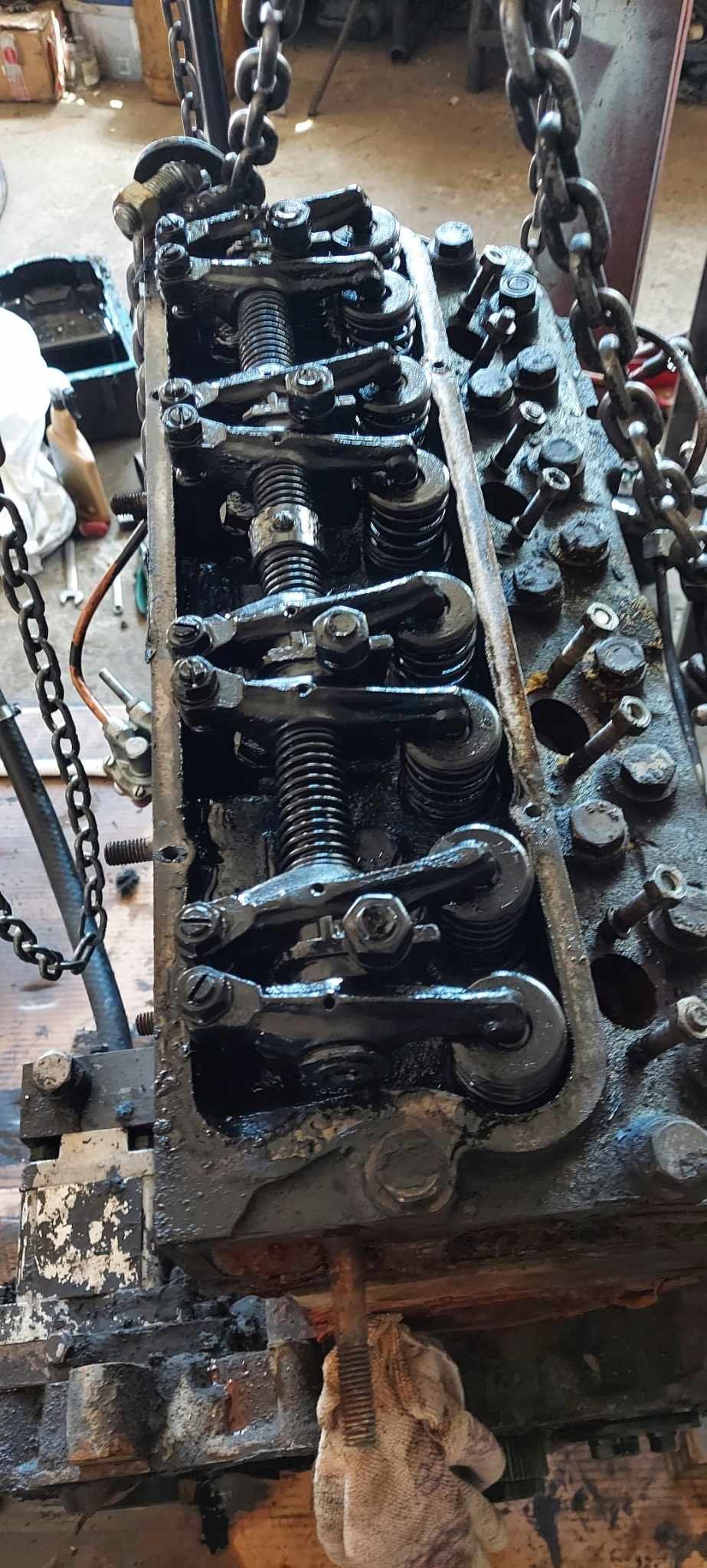 Głowica silnika wózka widłowego, widoczne sprężyny zaworowe i dźwigienki, podwieszona na łańcuchu. Detale mechaniczne, smar i ślady użytkowania.