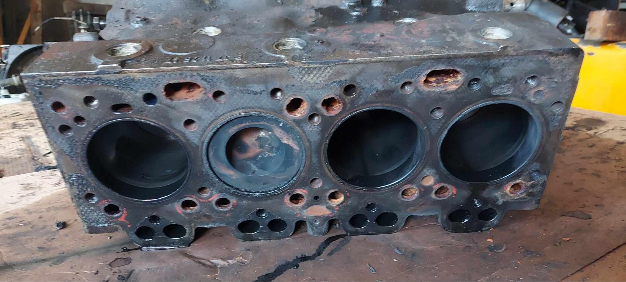 Zużyty blok silnika wózka widłowego z widocznymi śladami korozji i eksploatacji, po demontażu, leżący na warsztatowym stole. Widoczne otwory cylindrów.
