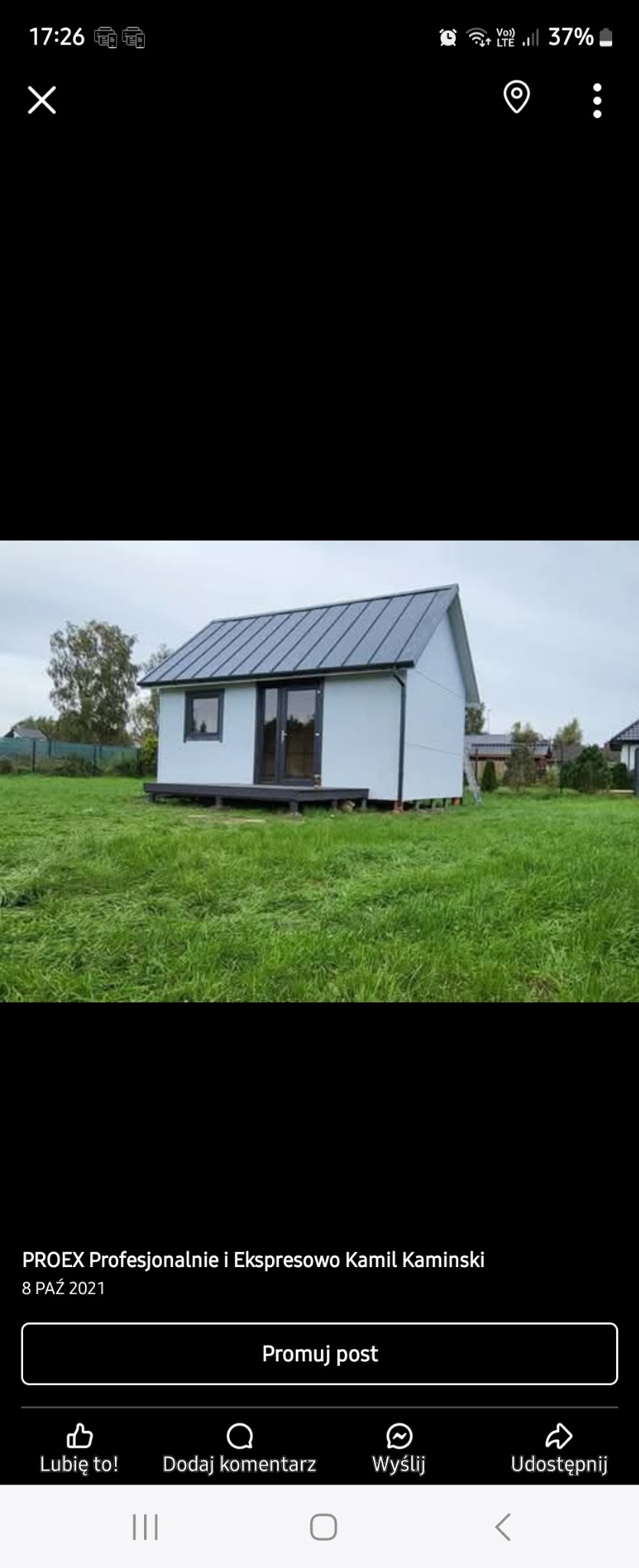 Gotowy, mały domek z dwuspadowym, grafitowym dachem na zielonej trawie, widok z przodu.