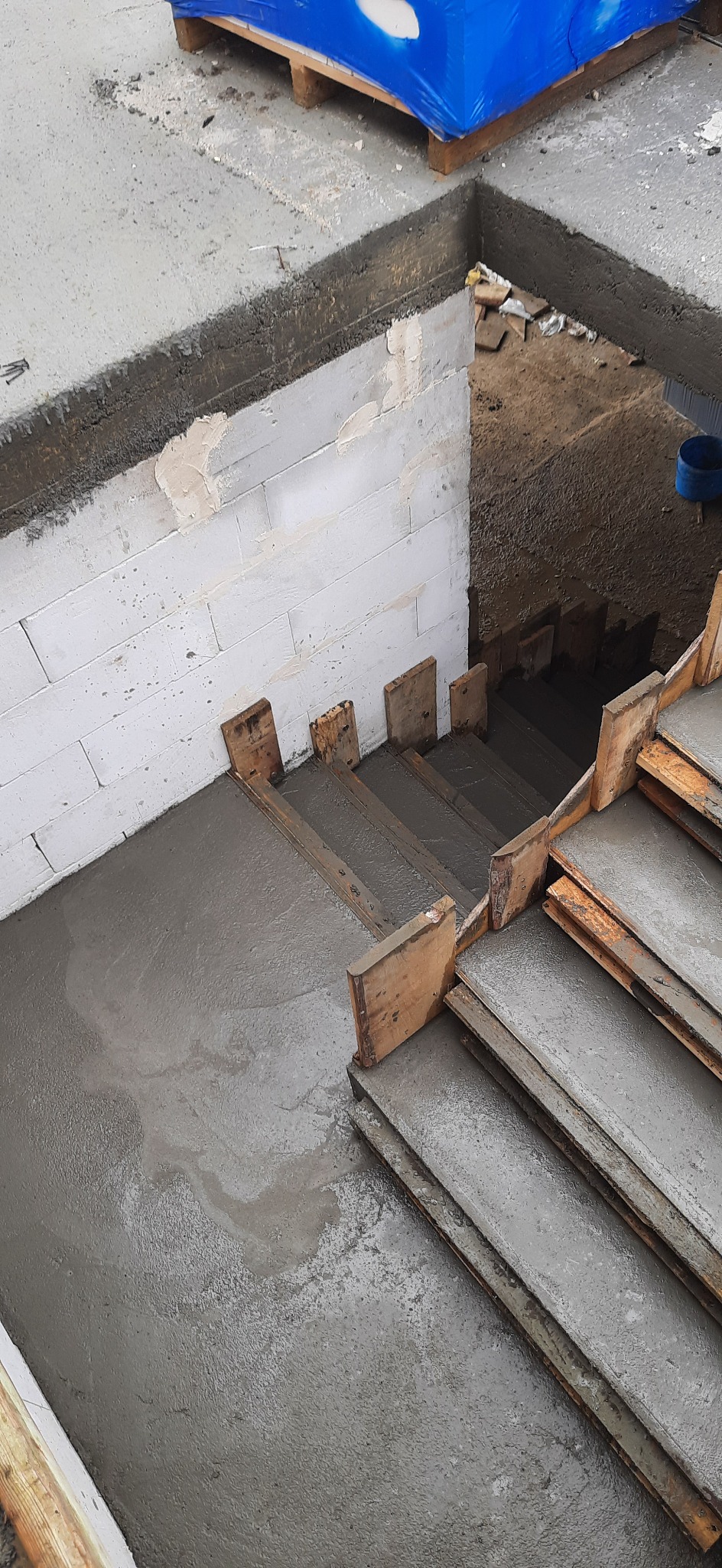 Świeżo wylany beton na schodach w trakcie budowy, widoczne szalunki drewniane i bloczki z betonu komórkowego.