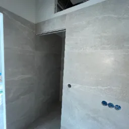 Ściana wyłożona płytkami imitującymi kamień, z widocznymi otworami na gniazdka elektryczne i fragmentem sufitu podwieszanego w trakcie montażu.