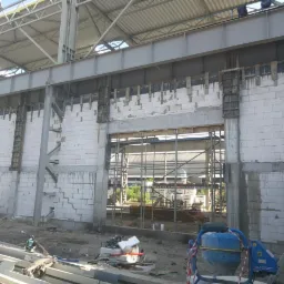 Wznoszenie ścian z betonu komórkowego w hali produkcyjnej, widoczne szalunki kolumn i stalowa konstrukcja dachu