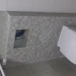 Wykończona łazienka z podwieszaną toaletą, szarą mozaiką na ścianie z ukrytym systemem spłukiwania i grzejnikiem drabinkowym.