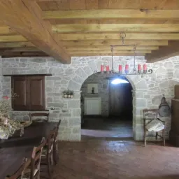 Rustykalne wnętrze z kamiennymi ścianami, drewnianym stropem belkowym i ceglaną podłogą w jodełkę, oświetlone żyrandolem z żarówkami w kształcie świec.